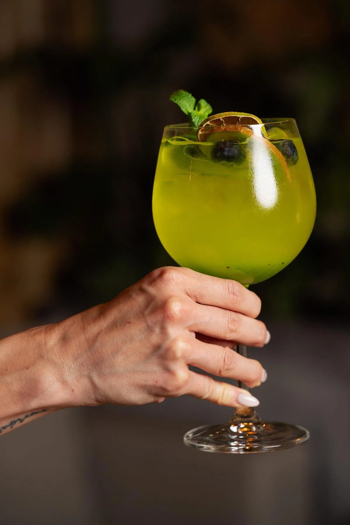 Un cocktail semnatura verde cu afine si citrice, tinut deasupra unei mese de lemn la Komodo Lounge
