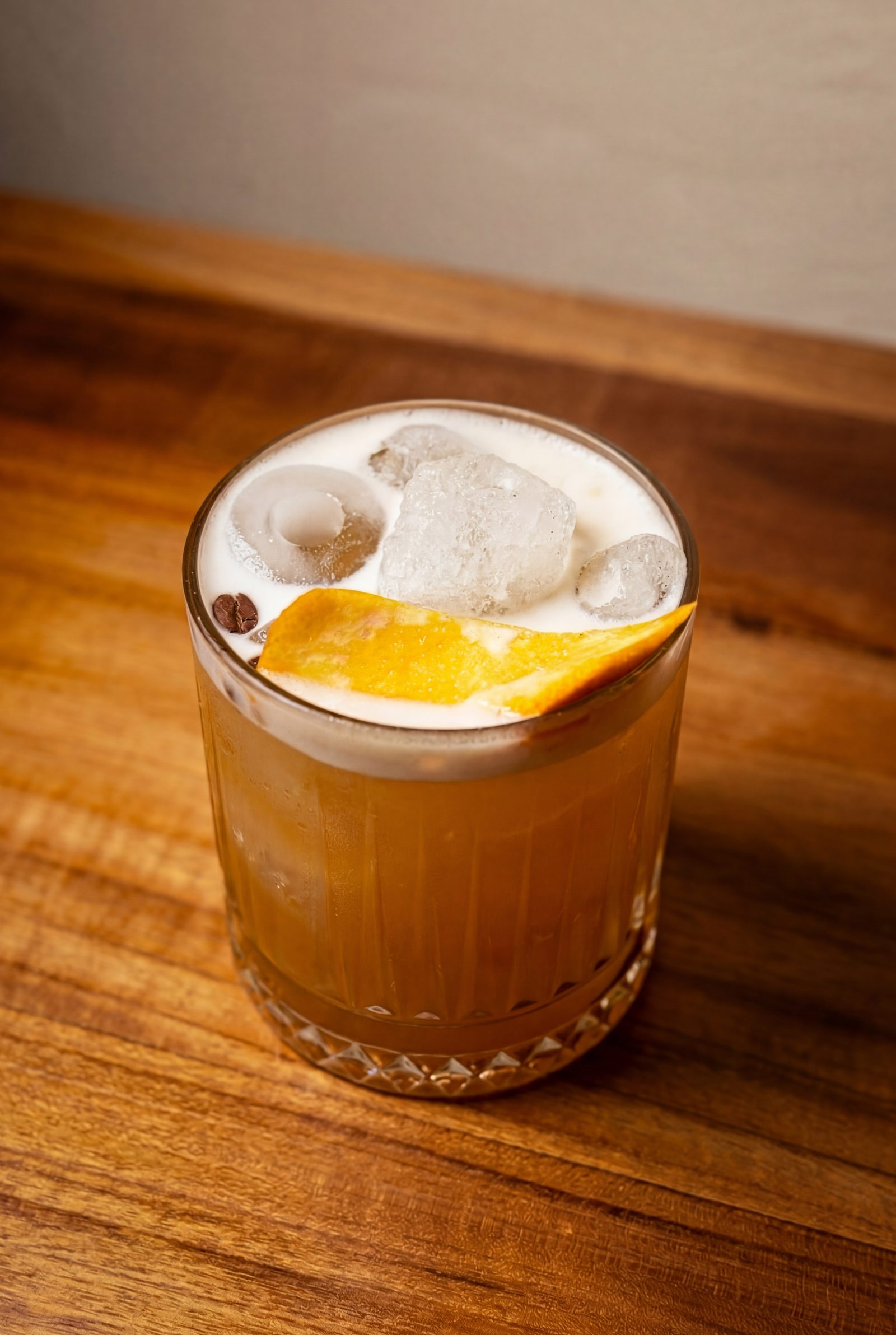 Signature amber cocktail with orange peel on a wood table